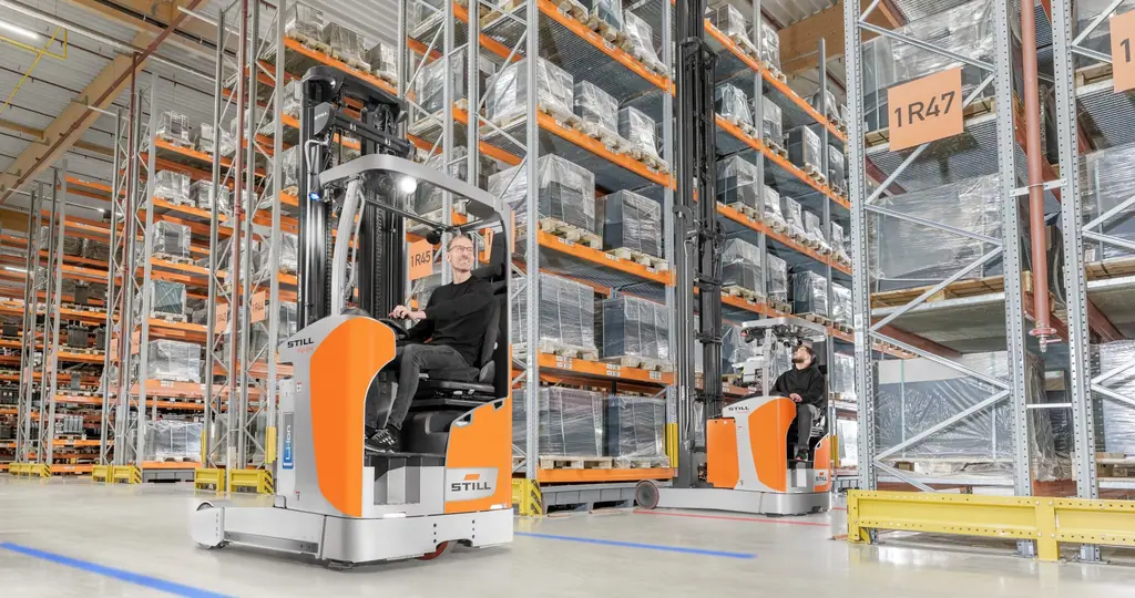 Raflı depoda çalışan STILL FM-X 14 reach truck ve operatörü; arka planda ikinci bir FM-X