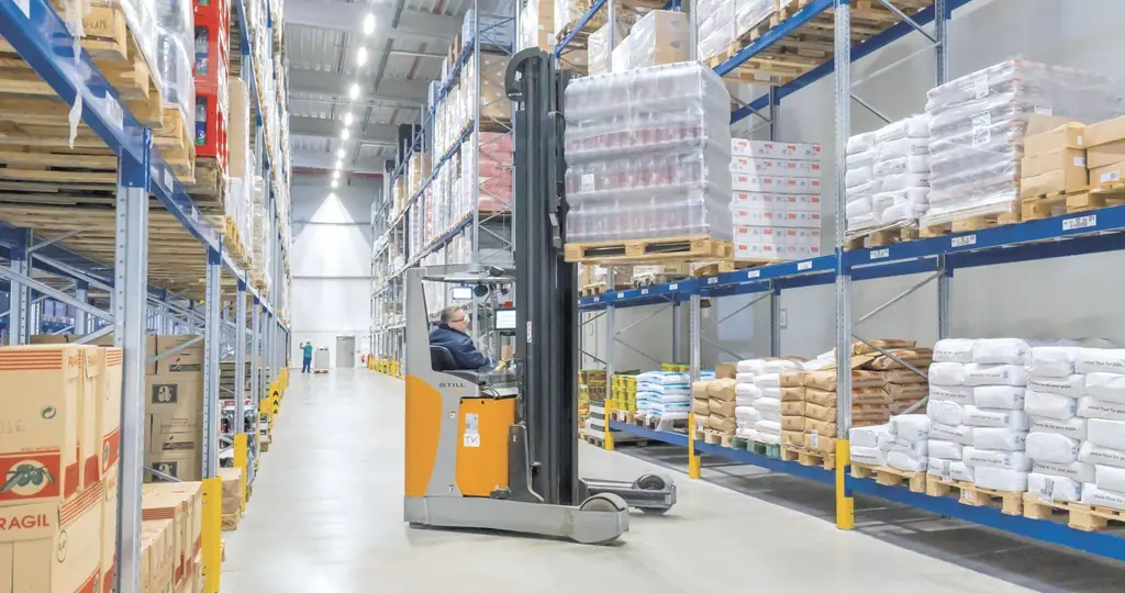 Raf koridorunda ilerleyen STILL FM-X reach truck ve operatörü