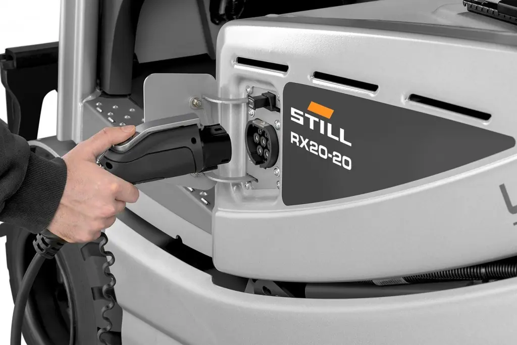 STILL RX 20-20'nin yan tarafındaki şarj soketine şarj fişi takılırken (isteğe bağlı yerleşik şarj cihazı; STILL'in 'RX-20_ON-Board-Charger' görseliyle aynı kare)