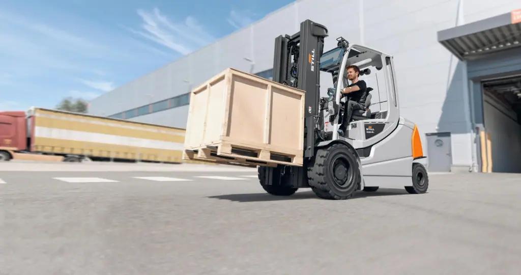 STILL RX 60-35/50 serisi forklift (RX60-45 Plus etiketli), depo önündeki açık sahada ahşap sandıkla hareket hâlinde