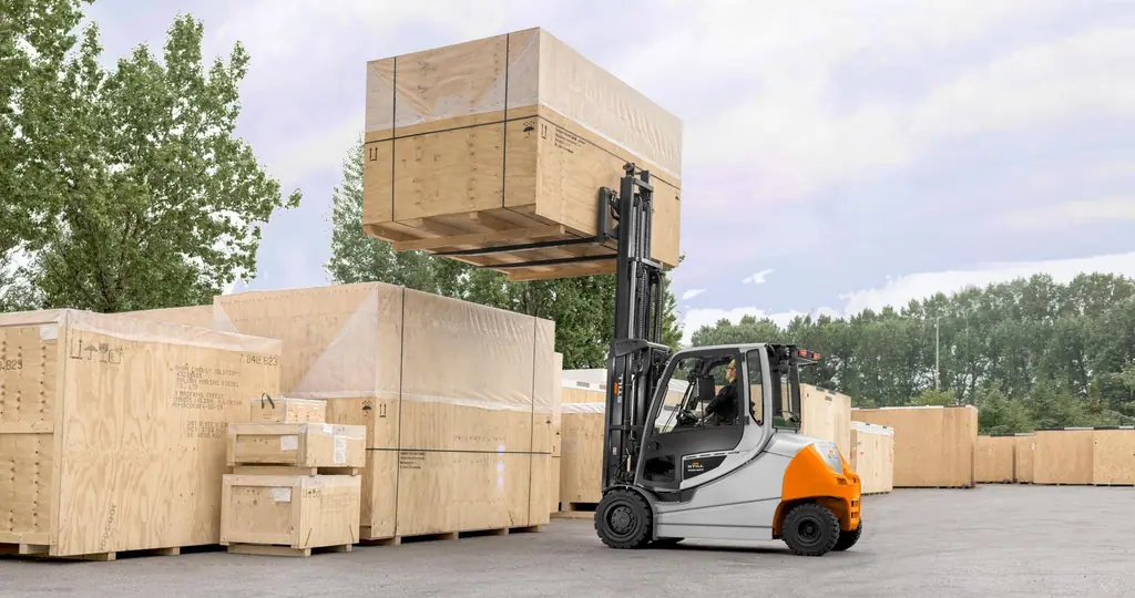 STILL RX 60-35/50 serisi akülü forklift, açık sahada büyük bir ahşap sandığı yükseğe kaldırırken