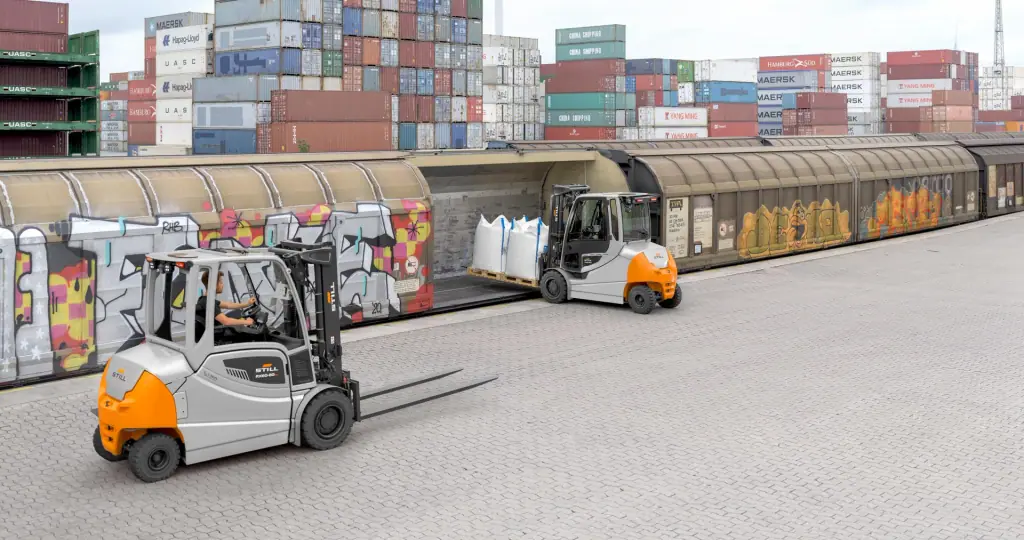 İki STILL RX 60-50 Plus forklift, konteyner sahasının önündeki demiryolu yükleme alanında; biri vagona big-bag yüklüyor