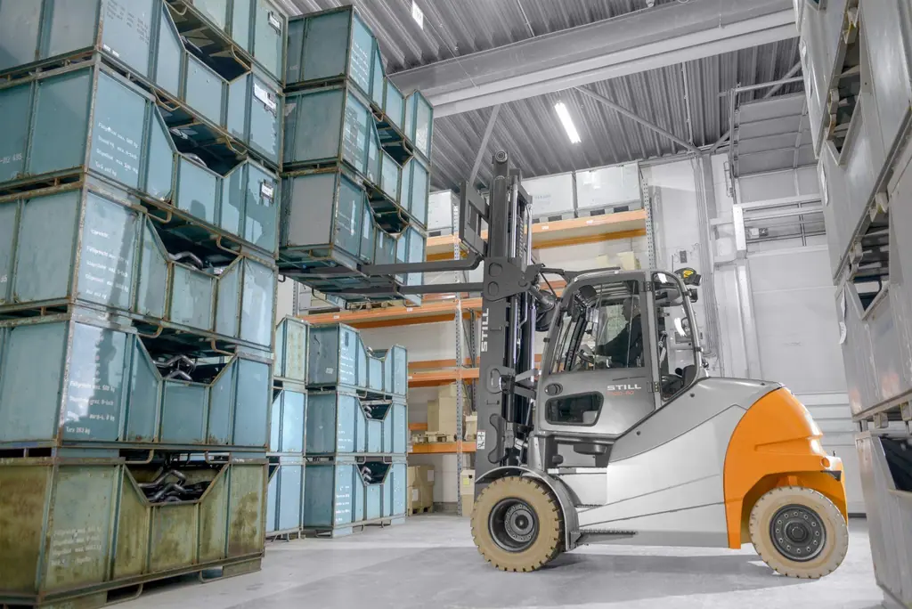 Depoda üst üste istiflenmiş metal kasaları kaldıran, tam kabinli STILL RX 60-80 akülü forklift