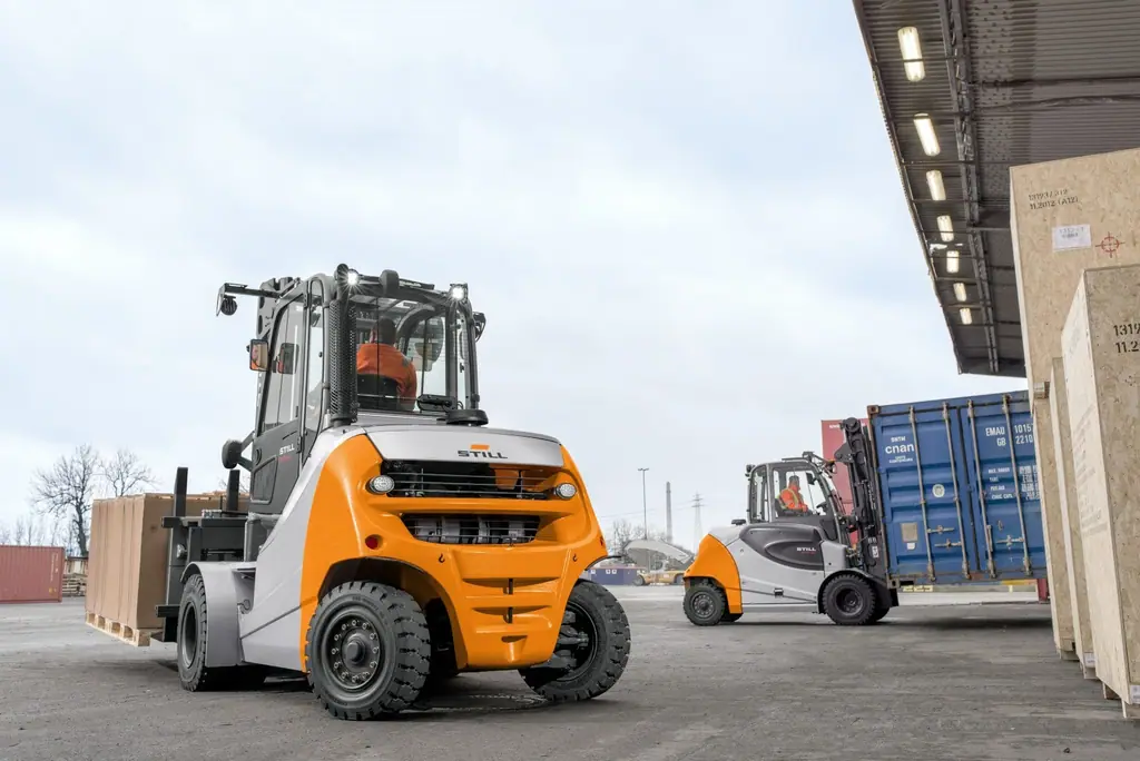 STILL RX 70 6,0–8,0 t serisi dizel forklift yük terminalinde büyük koli yüklü paletleri taşırken, arkadan görünüm; arka planda başka bir STILL forklift
