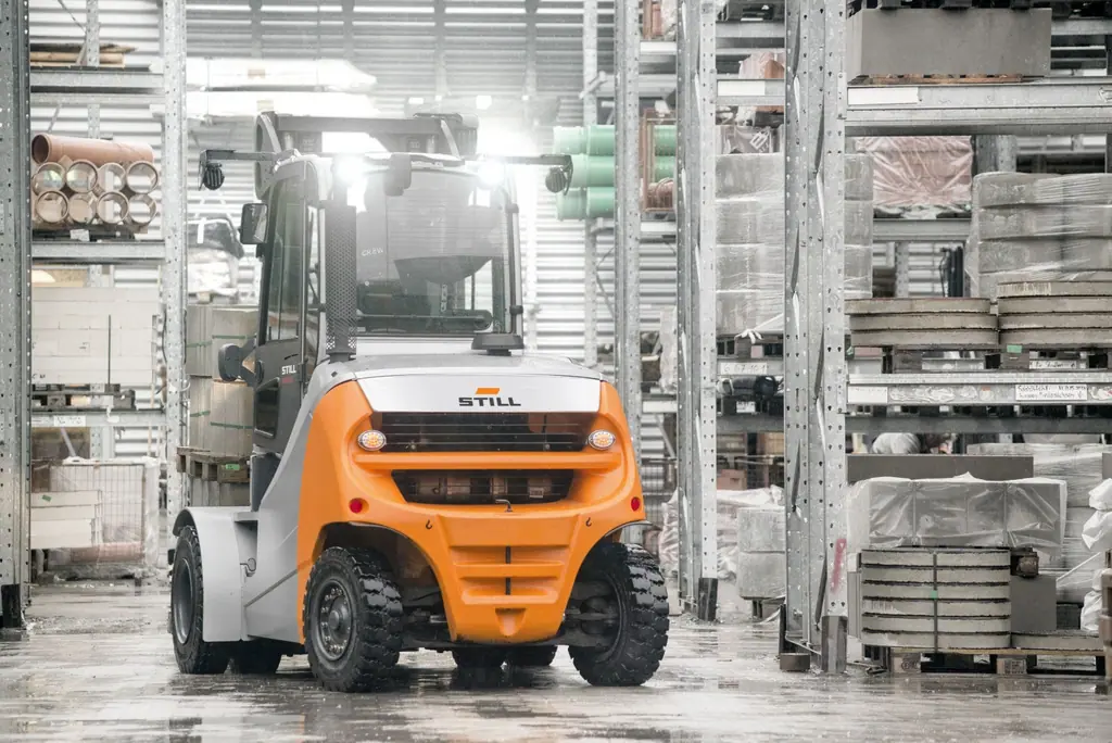 STILL RX 70 6,0–8,0 t serisi dizel forklift yapı malzemesi deposunda raf koridorunda, arkadan görünüm