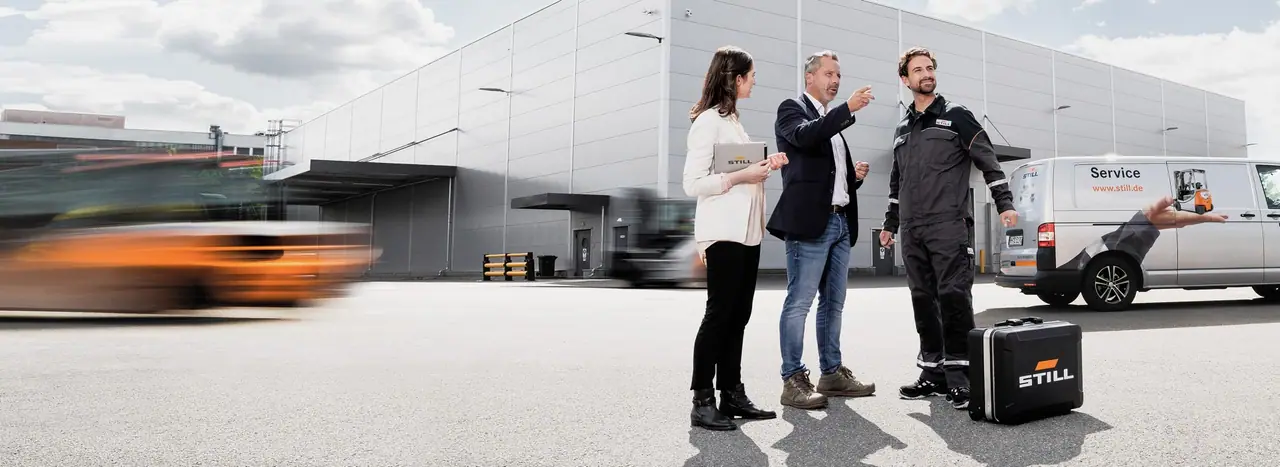 Depo önünde müşteriyle görüşen STILL servis teknisyeni ve satış danışmanı; arkada servis aracı